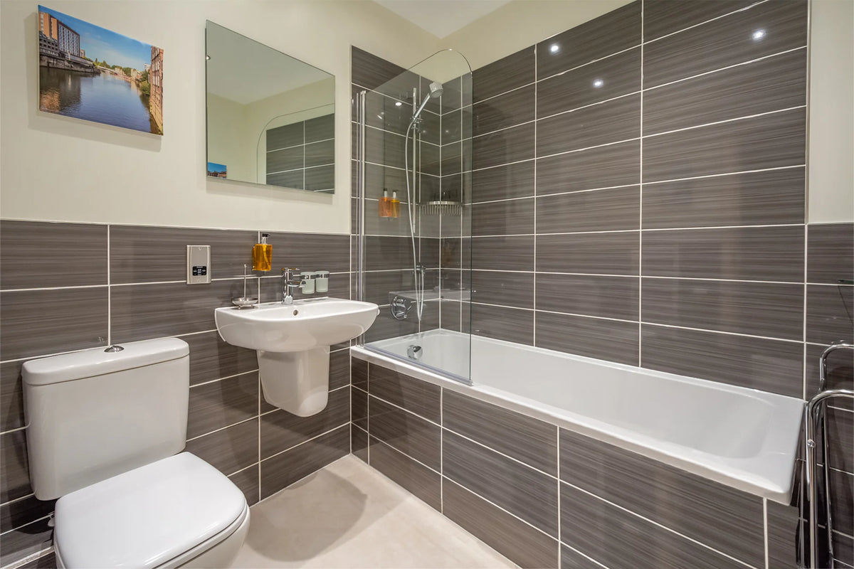 Hunter House Apartment bathroom with bath, shower and grey tiling in York city centre
