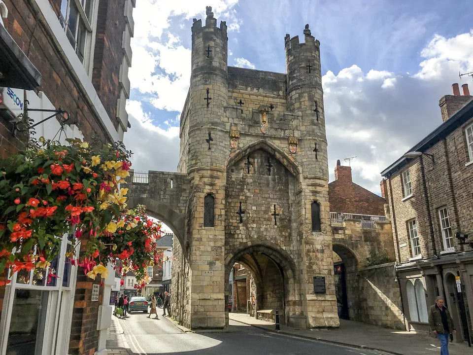 The stone towers and arch of Monk Bar seen from Goodramgate, with flowers in the foreground